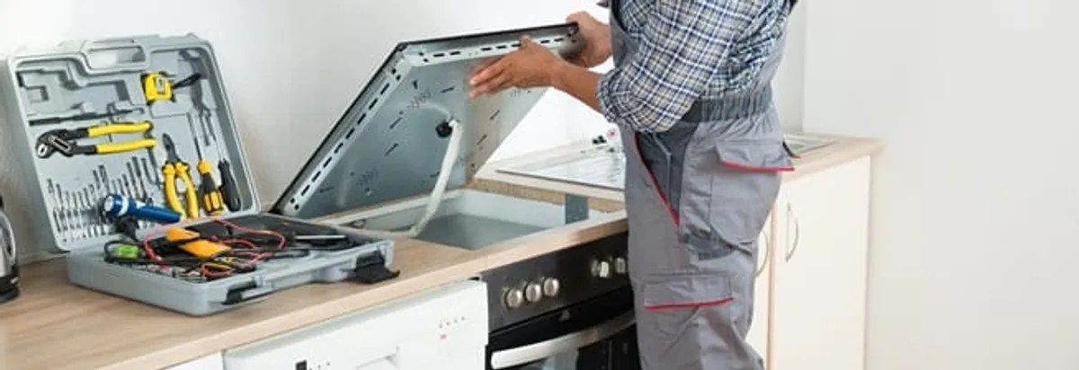 Cooktop repair technician lifting a built-in stovetop for service in Nashville, TN